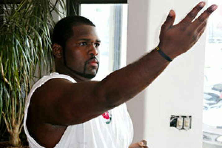 A man in a white sleeveless shirt reaching his arm out toward a wall.
